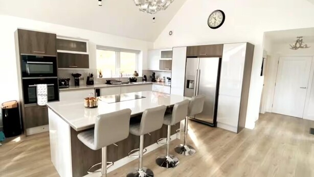 A modern kitchen with a central island, bar stools, built-in appliances, and a chandelier. - Camden House Holidays Scottish Highlands Villa (Spean Bridge)