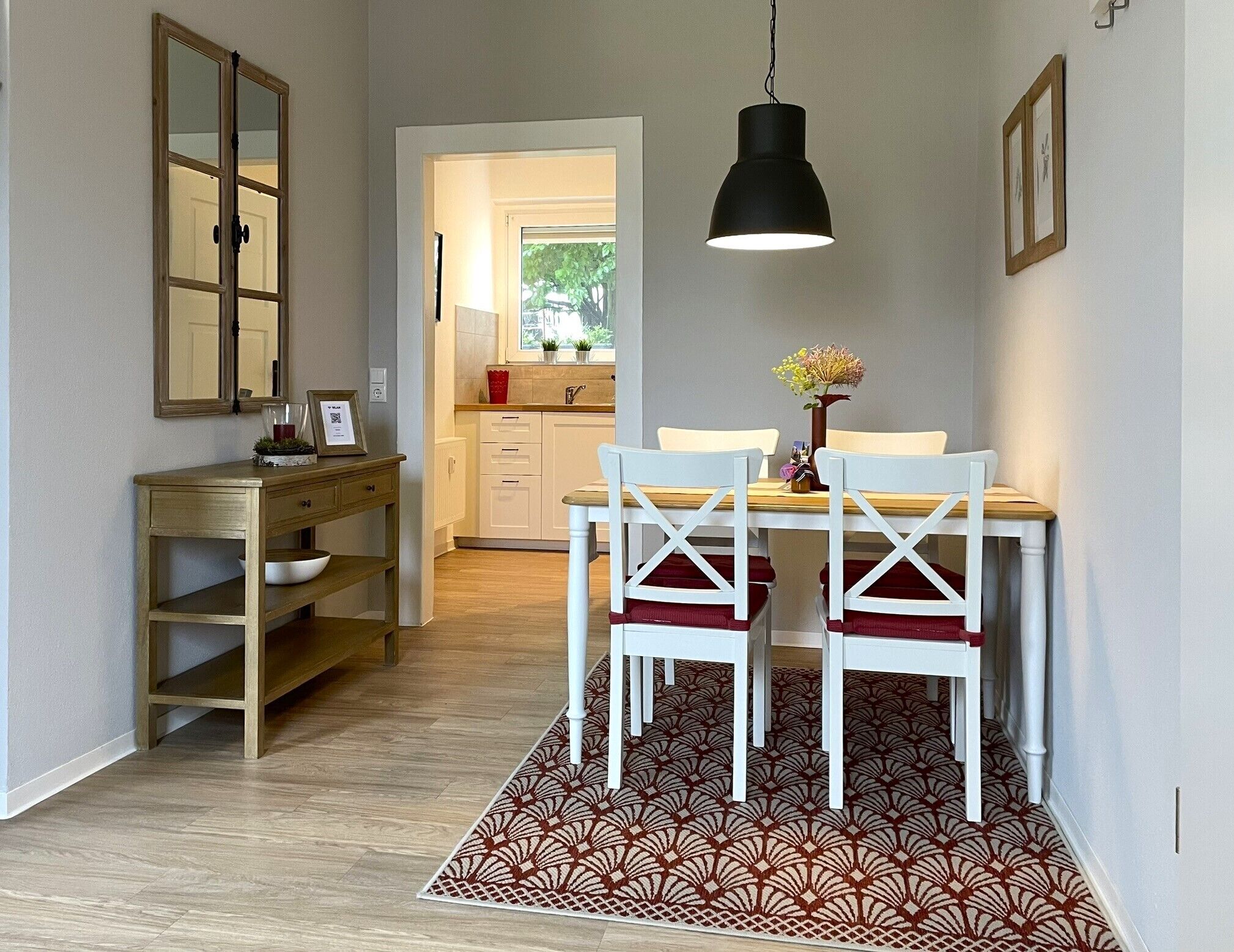 A dining area with a table, chairs, a hanging light fixture, a wooden console table, and a patterned rug.