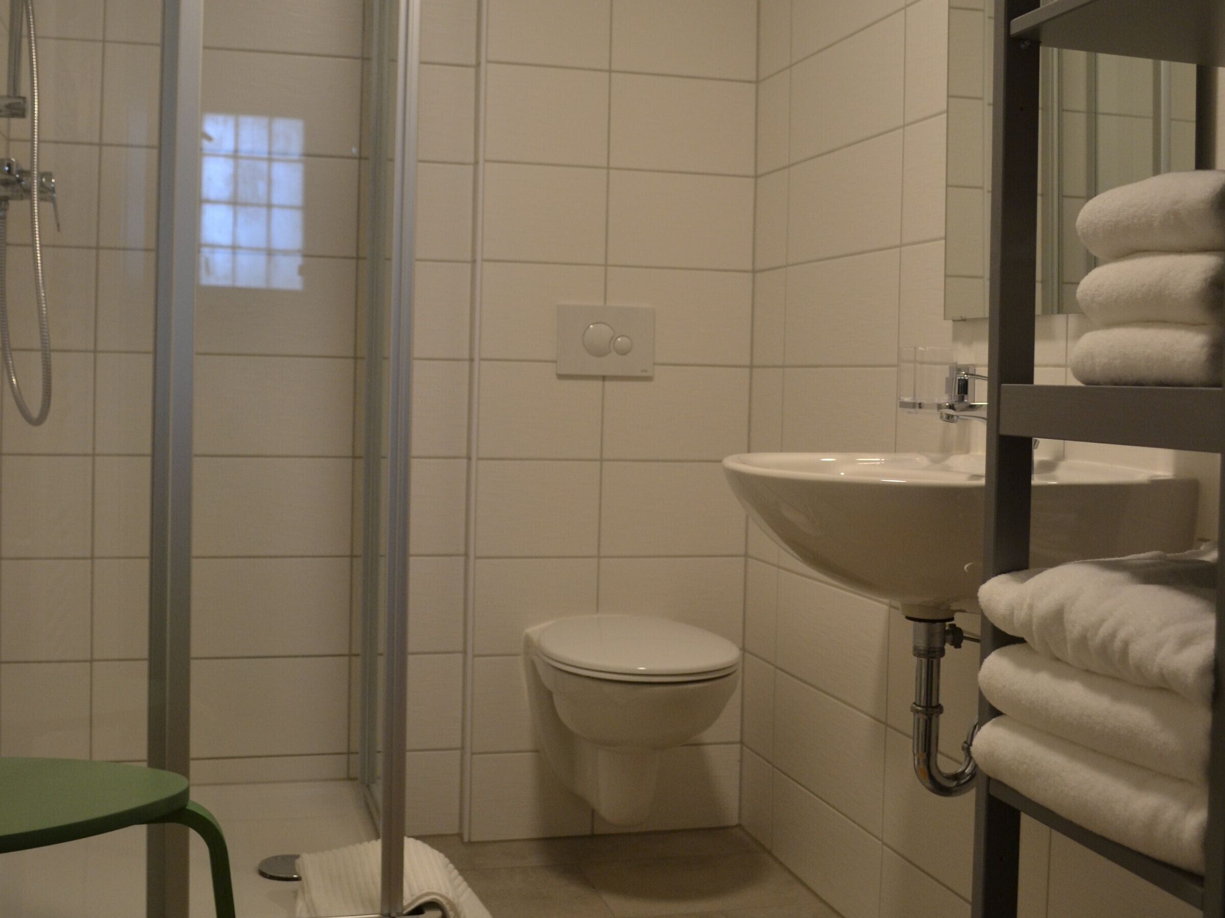 A bathroom with a shower, toilet, sink, and a green chair.
