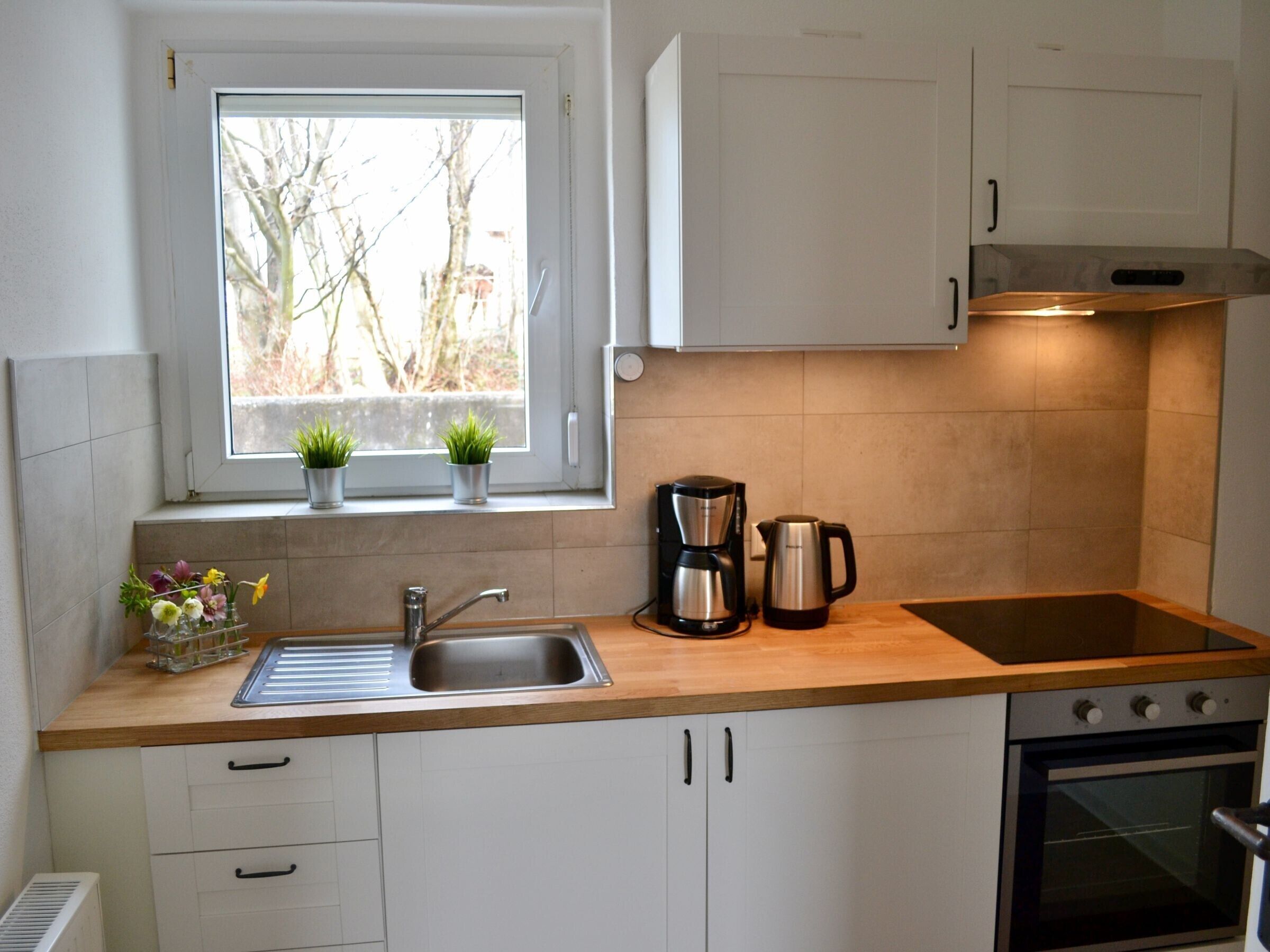 Cocina compacta con ventana, lavamanos, estufa y alacenas.