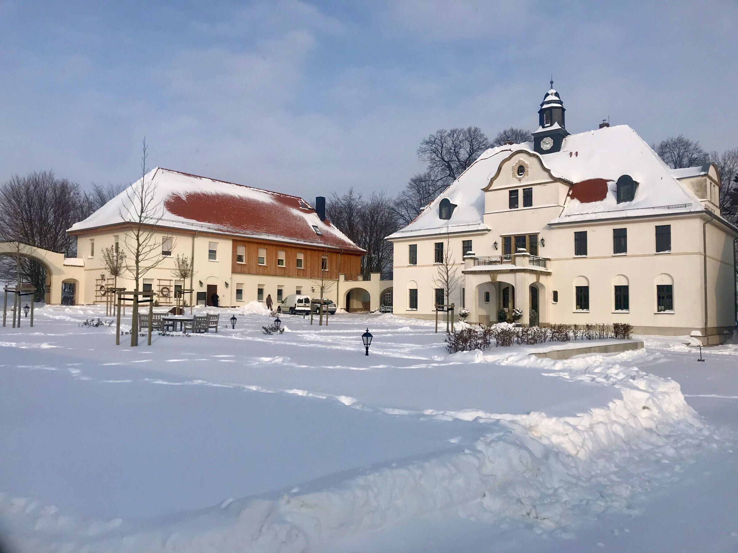 En stor byggnad med ett snötäckt tak, ett klocktorn och en innergård med bänkar och snö på marken.
