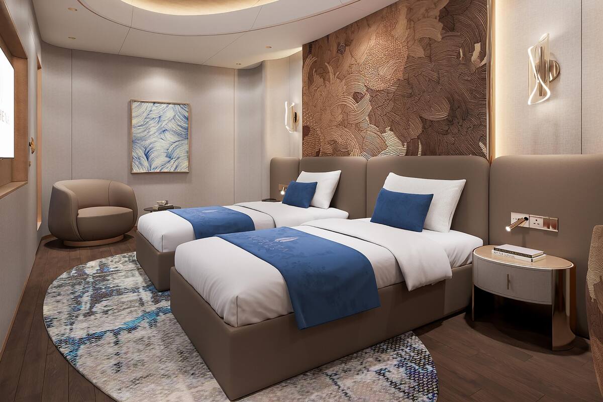 A modern hotel room with a curved ceiling, a large bed with blue and white bedding, a side table, and a wall-mounted light fixture.