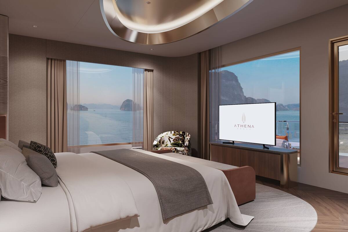 A modern hotel room with a large bed, a TV, and a view of the sea.