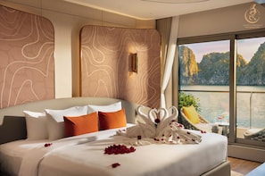 Habitación de hotel con cama, almohadas, un cisne decorativo hecho con toallas y vista a un cuerpo de agua con acantilados.