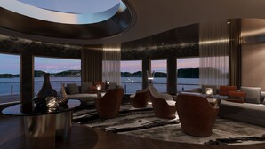 A modern interior with a curved ceiling, large windows with a view of the water, and contemporary furniture. - Athena Premium Cruise Halong Bay (Bai Chay)