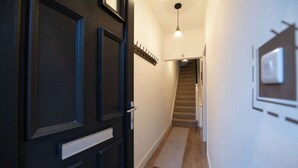 A hallway with a dark wooden door, a coat rack, a light fixture, a carpet, and a staircase. - Monks Quarters-Luxe 3 Bed, Private Parking x2 Cars (Lincolnshire)