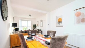 A dining area with a wooden table set for four, surrounded by chairs, a lamp, and framed artwork on the walls. - Monks Quarters-Luxe 3 Bed, Private Parking x2 Cars (Lincolnshire)