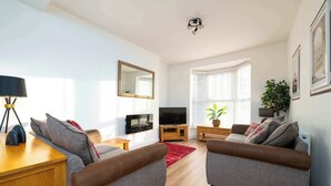 A modern living room with two grey sofas, a wooden coffee table, a flat-screen TV, a mirror, and a potted plant. - Monks Quarters-Luxe 3 Bed, Private Parking x2 Cars (Lincolnshire)