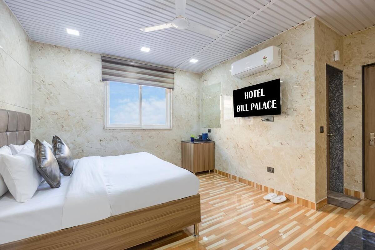 A hotel room with a bed, a TV mounted on the wall, a window, and a door.