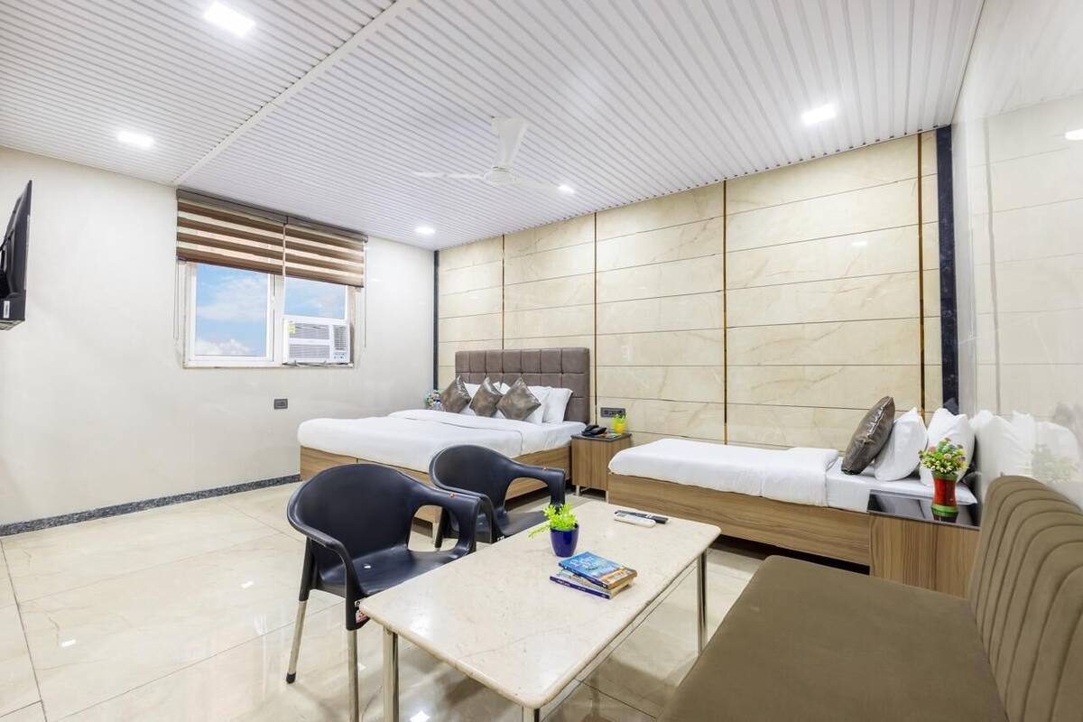 A hotel room with a bed, a sofa, a dining table, and a TV mounted on the wall.