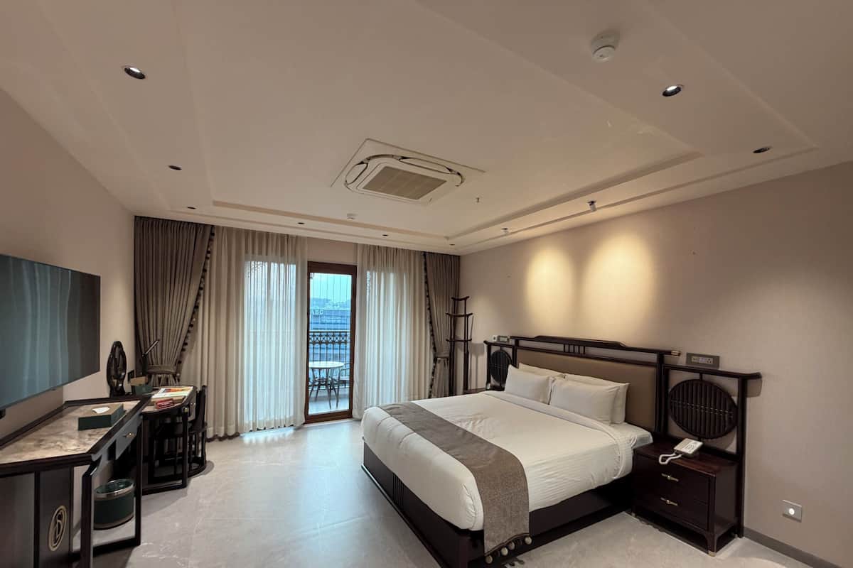 Una habitación de hotel moderna con una cama grande, un escritorio con una silla, un televisor y un balcón con cortinas.
