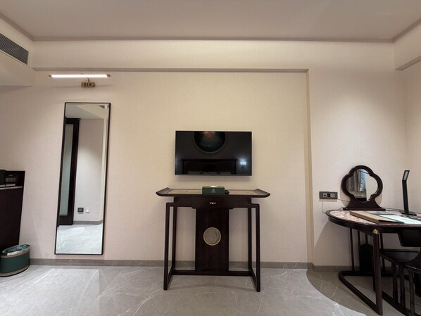 Habitación de hotel con una televisión de pantalla plana montada en la pared, un pequeño escritorio de madera con espejo y un cesto de basura.