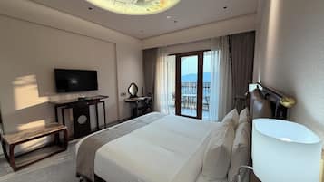 Habitación de hotel con cama, televisión, escritorio, silla, lámpara y vistas al exterior.