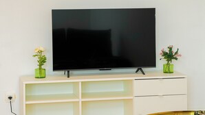 A television on a white stand with two small green vases on either side. - Cozy 1BR With Living Room Near City (Ghent)
