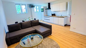 Una sala moderna con un sofá seccional, una mesa de centro de vidrio y una cocina al fondo.