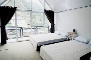 Habitación de hotel con dos camas, una mesita de noche y vistas a un paisaje montañoso a través de amplias ventanas.
