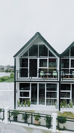 A two-story building with large windows and balconies, featuring outdoor seating and potted plants.