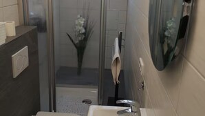 Un baño moderno con cabina de ducha de vidrio, inodoro, lavamanos con dispensador de jabón y espejo.