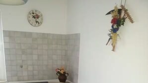 Un rincón comedor con mantel azul, sillas de madera, un jarrón con flores y un reloj en la pared.