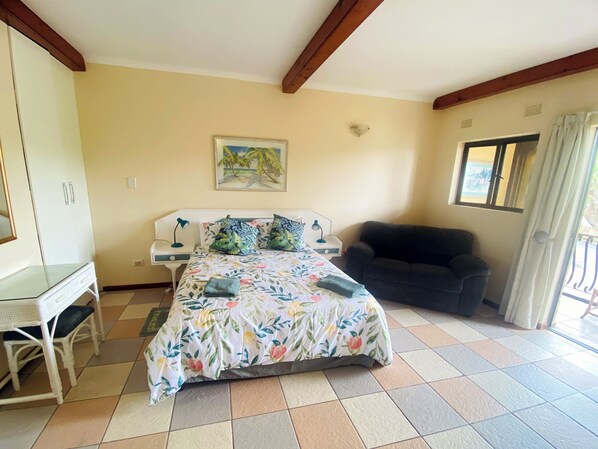 Une chambre à coucher avec un lit, un bureau, une chaise, un canapé et une fenêtre avec des rideaux.