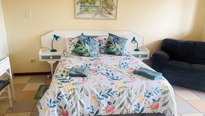 A neatly made bed with floral bedding, two bedside lamps, a nightstand, a couch, and a painting of a beach scene on the wall. - Crayfish Inn no'1 (Ramsgate)