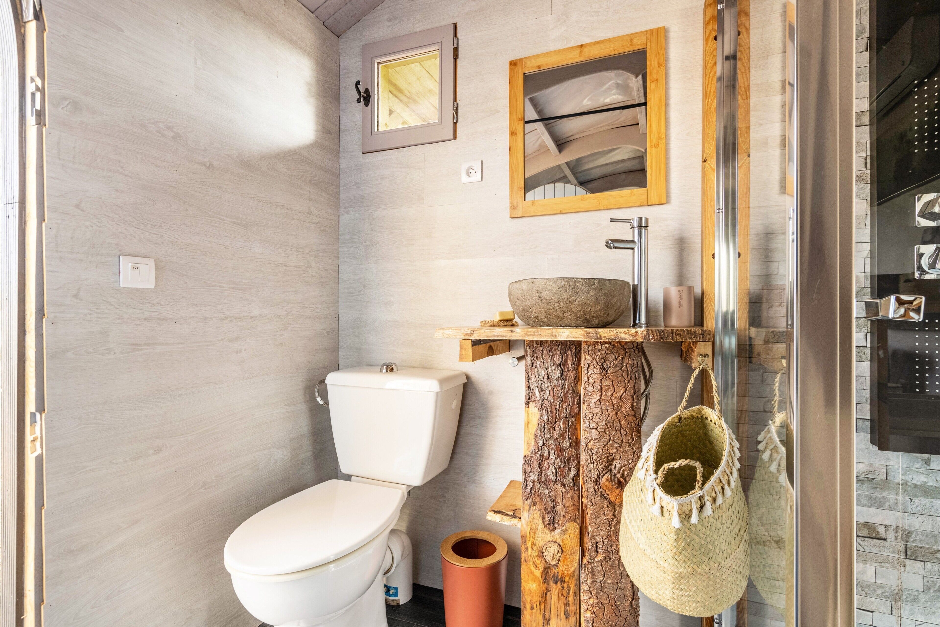 Ein Badezimmer mit Toilette, einem Holzwaschtisch, einem Steinsinkensowie einem hängenden Korb.