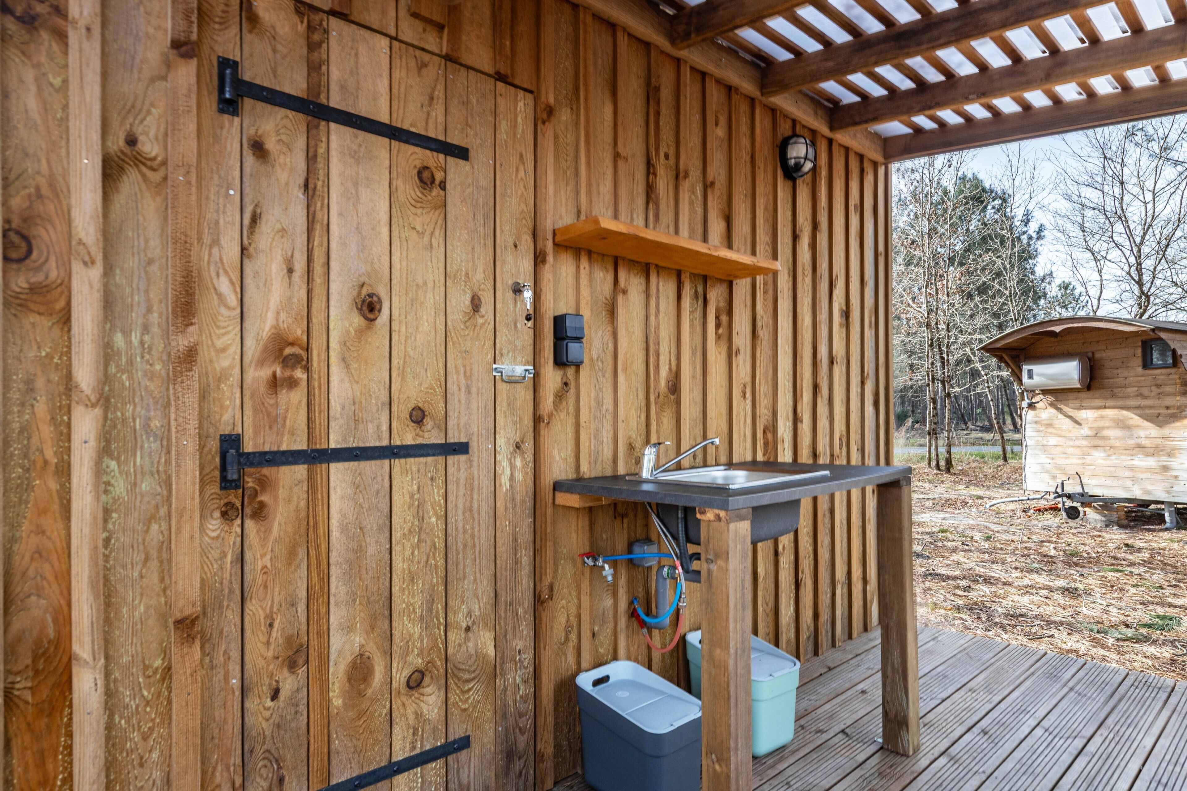 A wooden cabin with a built-in sink, a shelf, and a door with a black handle.