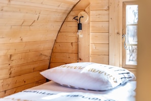 A wooden interior with a bed, a pillow, a light fixture, and a window. - Le Tonneau des Chouchous (Hourtin)