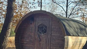 A wooden barrel-shaped structure with a hexagonal door, surrounded by trees and dry leaves.