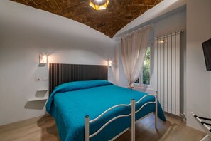 A bedroom with a bed, a sloped ceiling, a window with curtains, and a radiator.