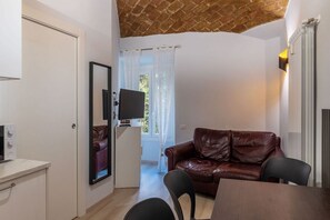 A compact living space with a brown leather sofa, a dining table, a white cabinet, and a television mounted on the wall.