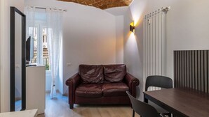 A room with a brown leather sofa, a dining table, and a wall-mounted light fixture. - GuestHost - A modern and welcoming 55 square meters apartment, perfect for four people, located on the ground floor of a building with an elevator (NOT accessible for disabled guests and not necessary to access the apartment). The property is just steps  (Rome)