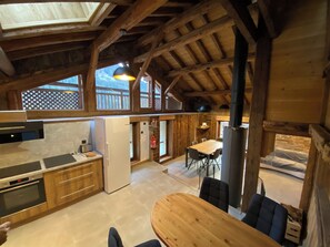 A spacious kitchen with wooden beams, a dining area with a round table, and a large window overlooking a wooden deck. - Chalet L'orsett, south-facing with mountain views, resort center, quiet area! (Champagny-en-Vanoise)