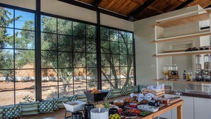 Un desayuno dispuesto con una mesa, asientos y vistas a árboles a través de grandes ventanales.