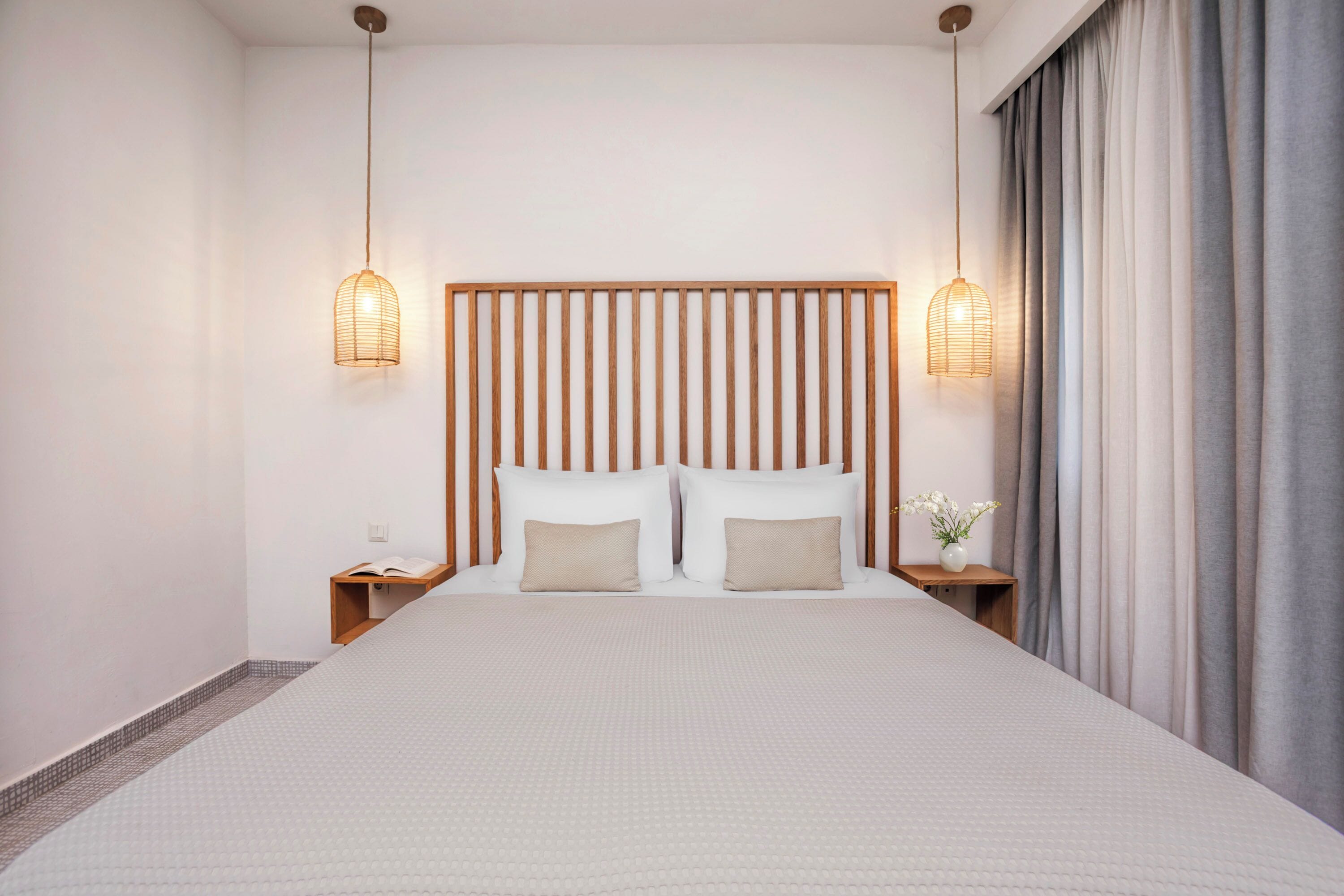 A modern hotel room with a large bed, wooden headboard, bedside tables, and a nightstand with a lamp.