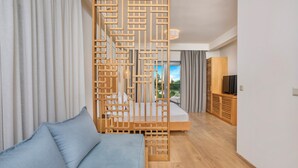 Habitación de hotel moderna con un separador de madera, un sofá, una cama, un televisor y vistas al exterior.
