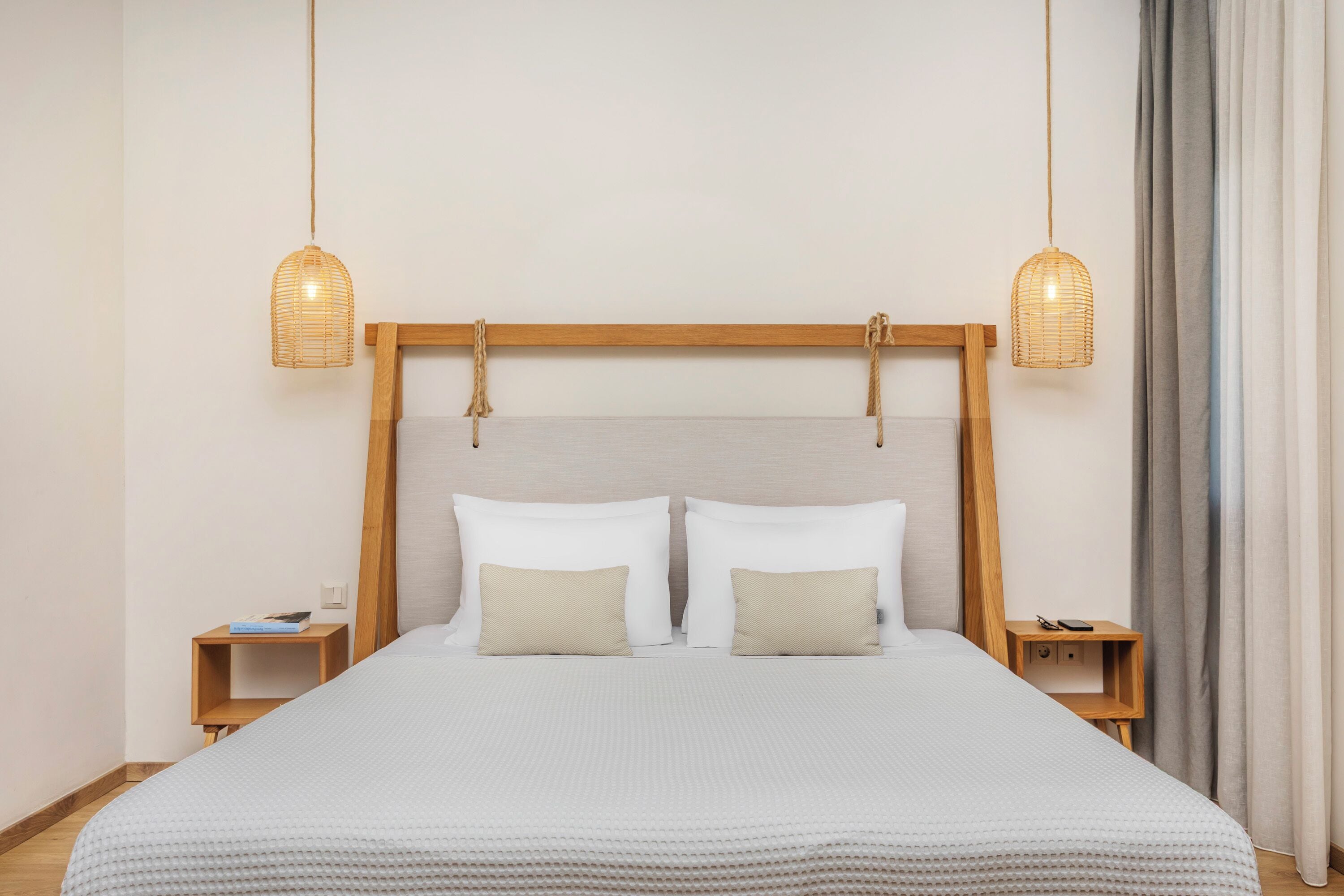 A neatly made bed with a wooden headboard, two bedside tables, and two hanging wicker lamps.