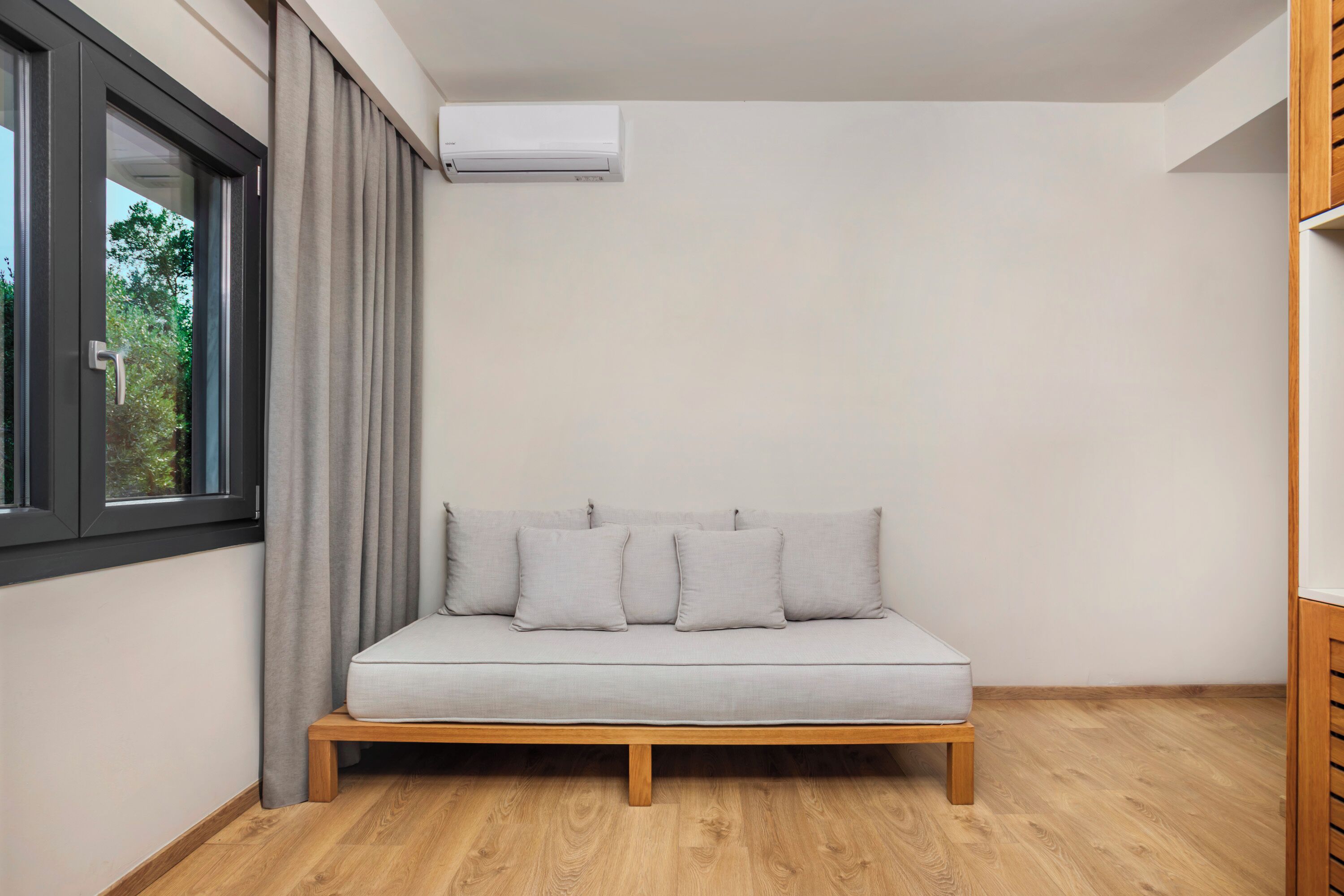 A modern room with a grey sofa, wooden floor, and a window with curtains.