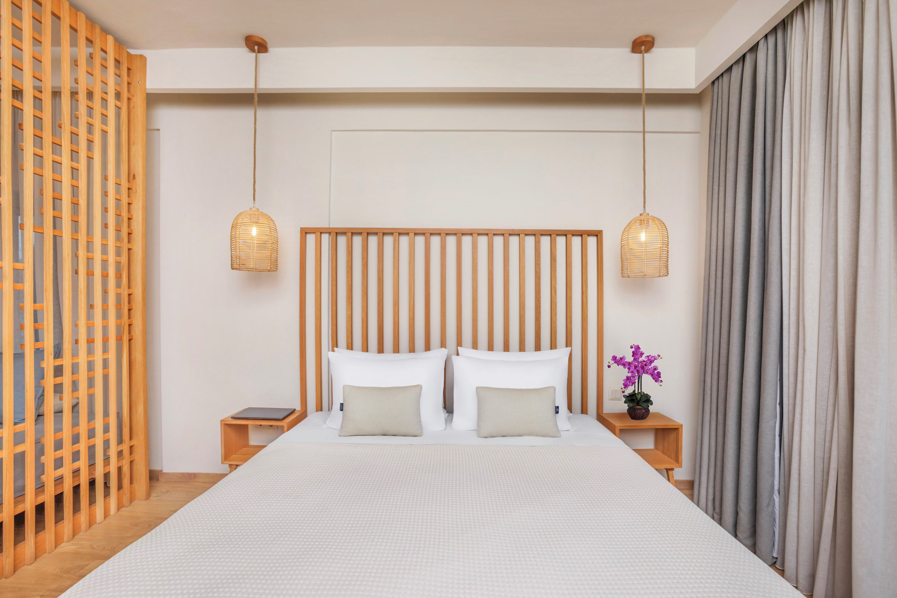 A modern hotel room with a large bed, two bedside tables, a wooden headboard, and two hanging lamps.