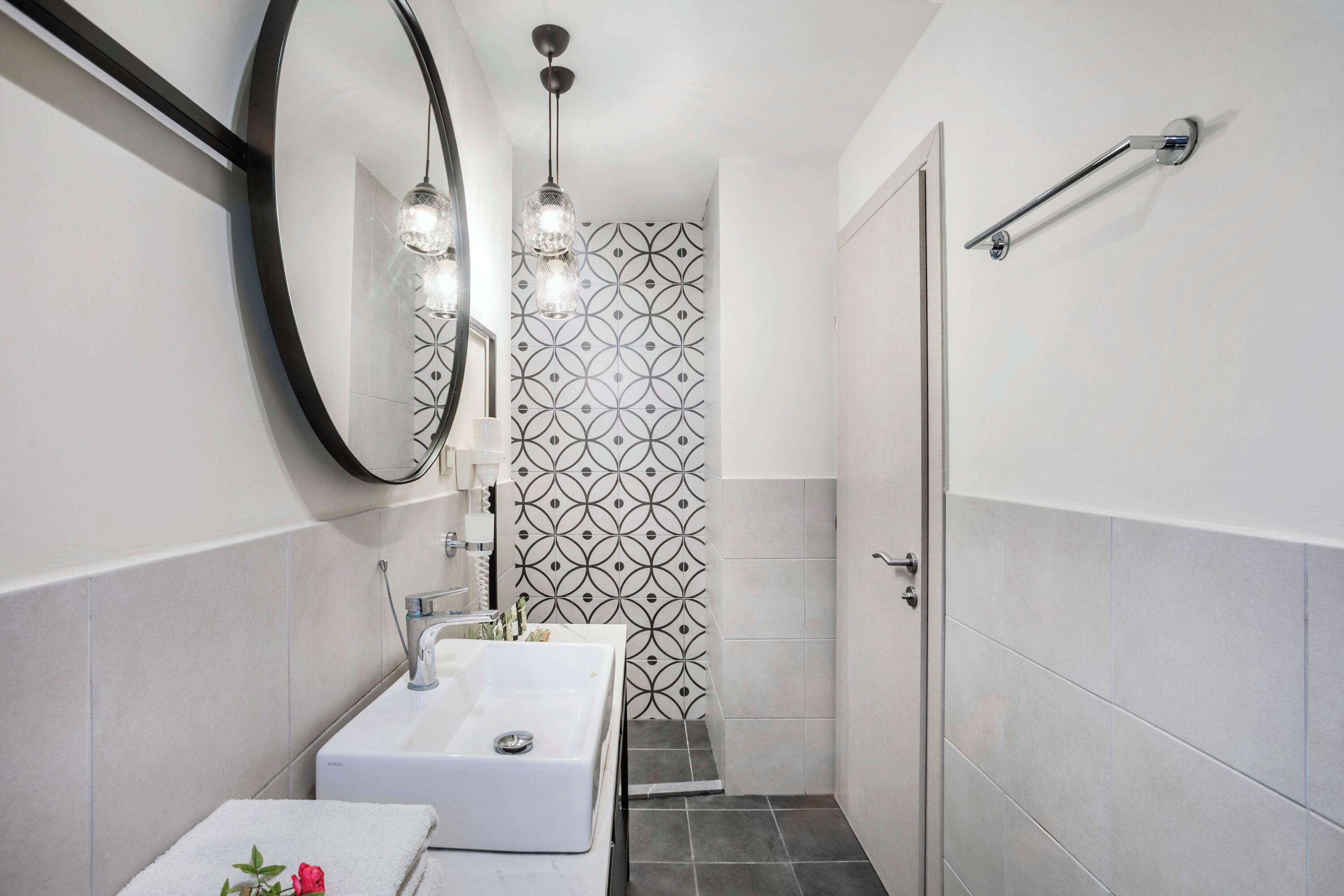 A modern bathroom with a large mirror, two sinks, a towel rack, and a shower area.