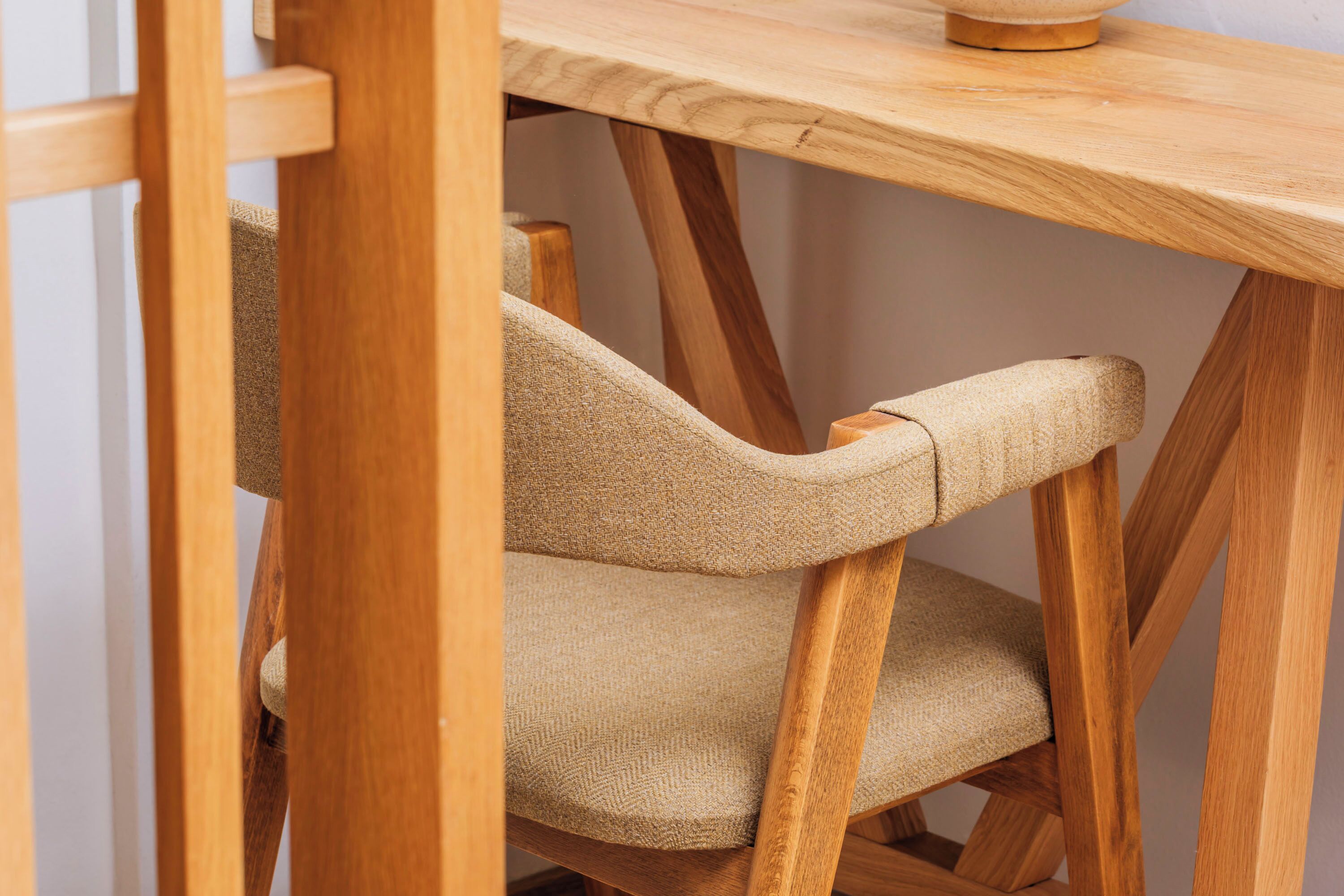Una silla de madera con asiento y respaldo texturizados, ubicada debajo de una mesa de madera.