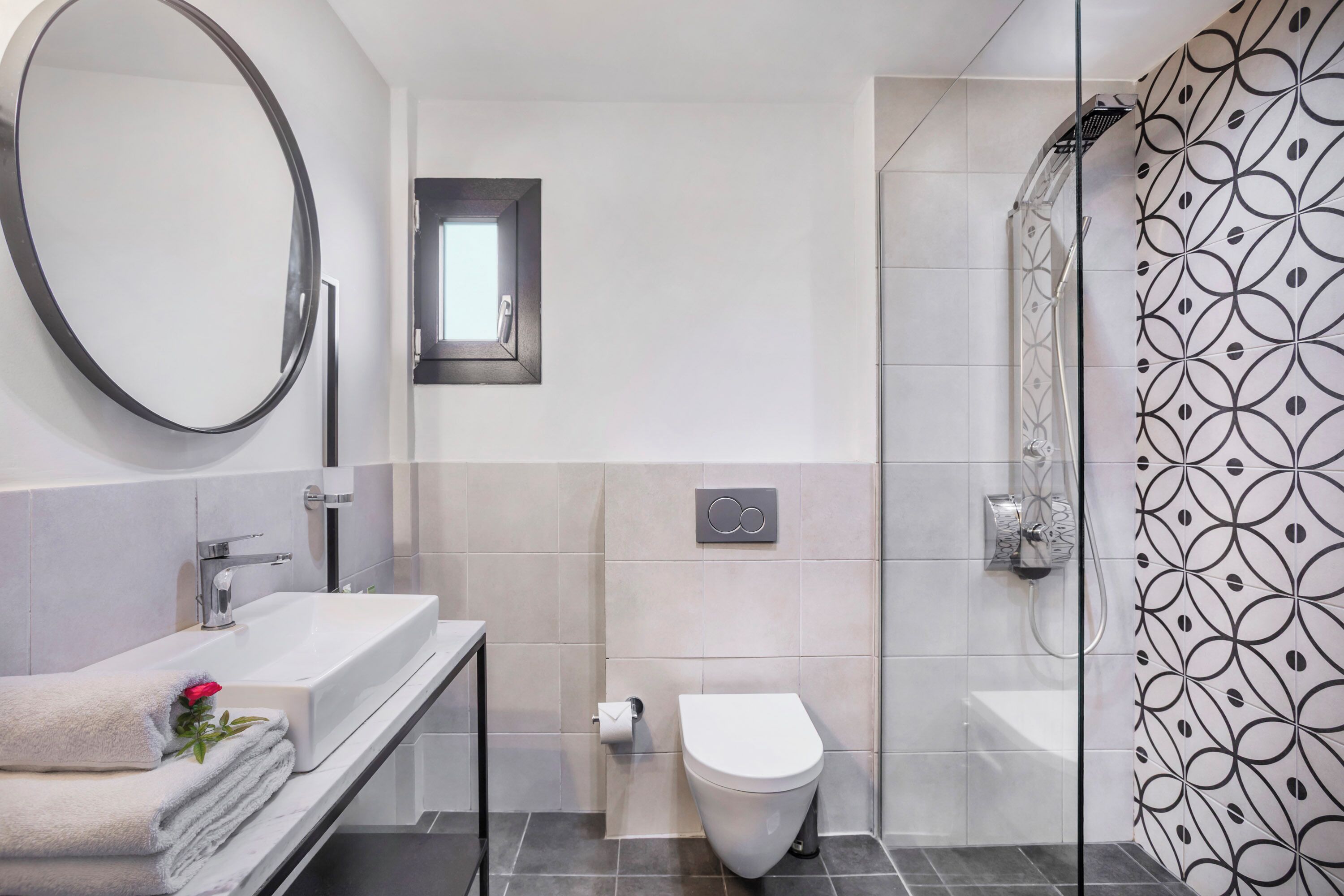 Un baño moderno con un espejo redondo, un lavamanos blanco, un inodoro y una zona de ducha.