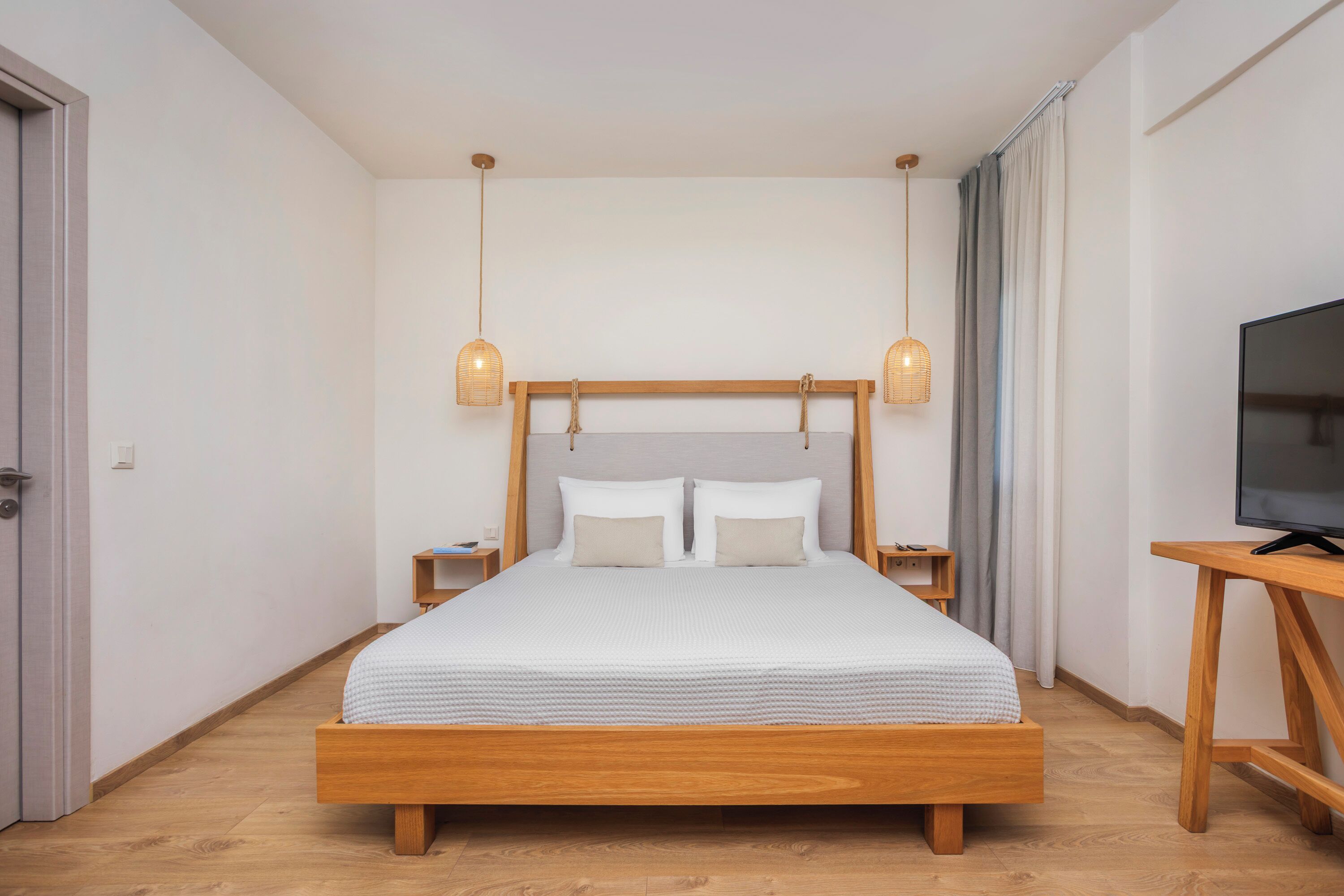 A modern bedroom with a wooden bed, bedside tables, a TV, and hanging lamps.