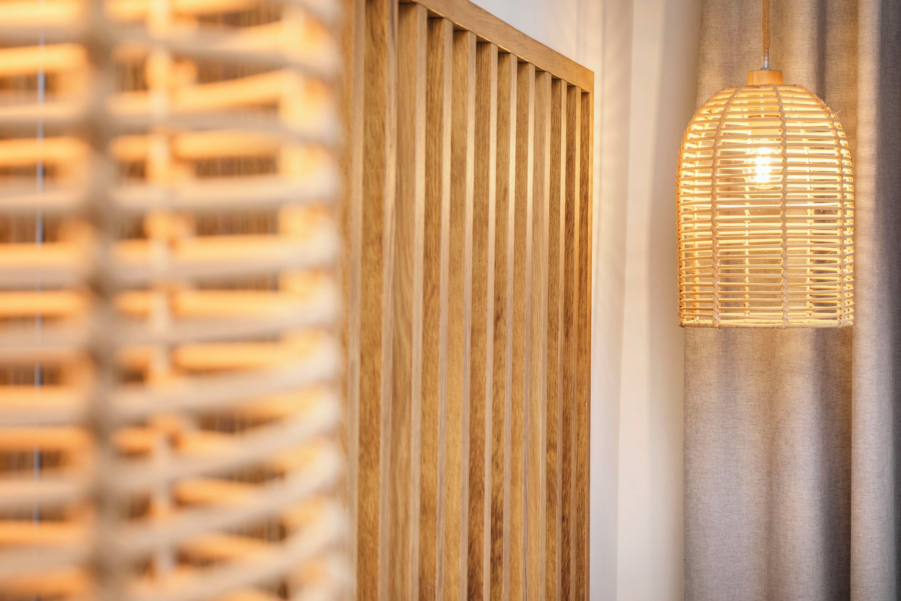 A modern interior with a vertical wooden slat wall and a woven rattan pendant light.