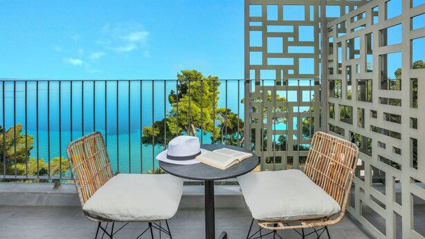 Un balcón con dos sillas de mimbre, una mesa y vista al mar.