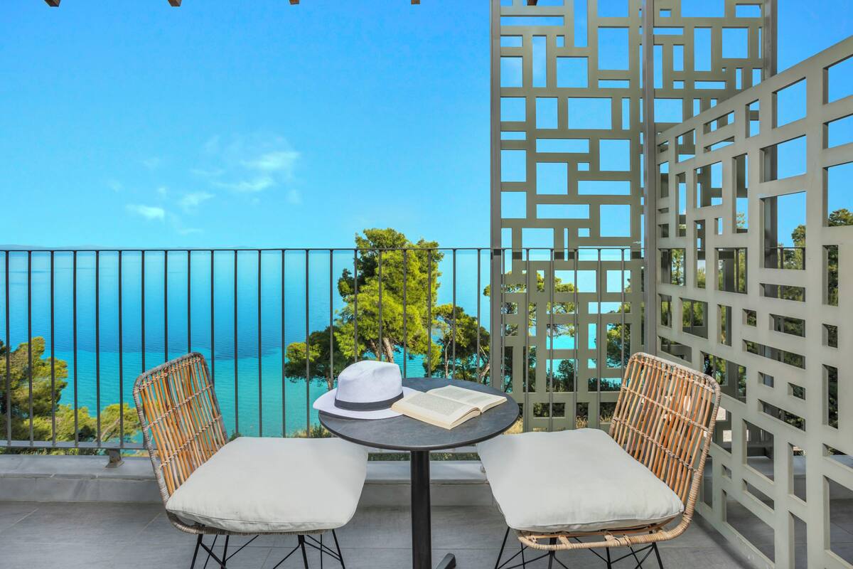 Un balcón con dos sillas de mimbre, una mesa y vista al mar.