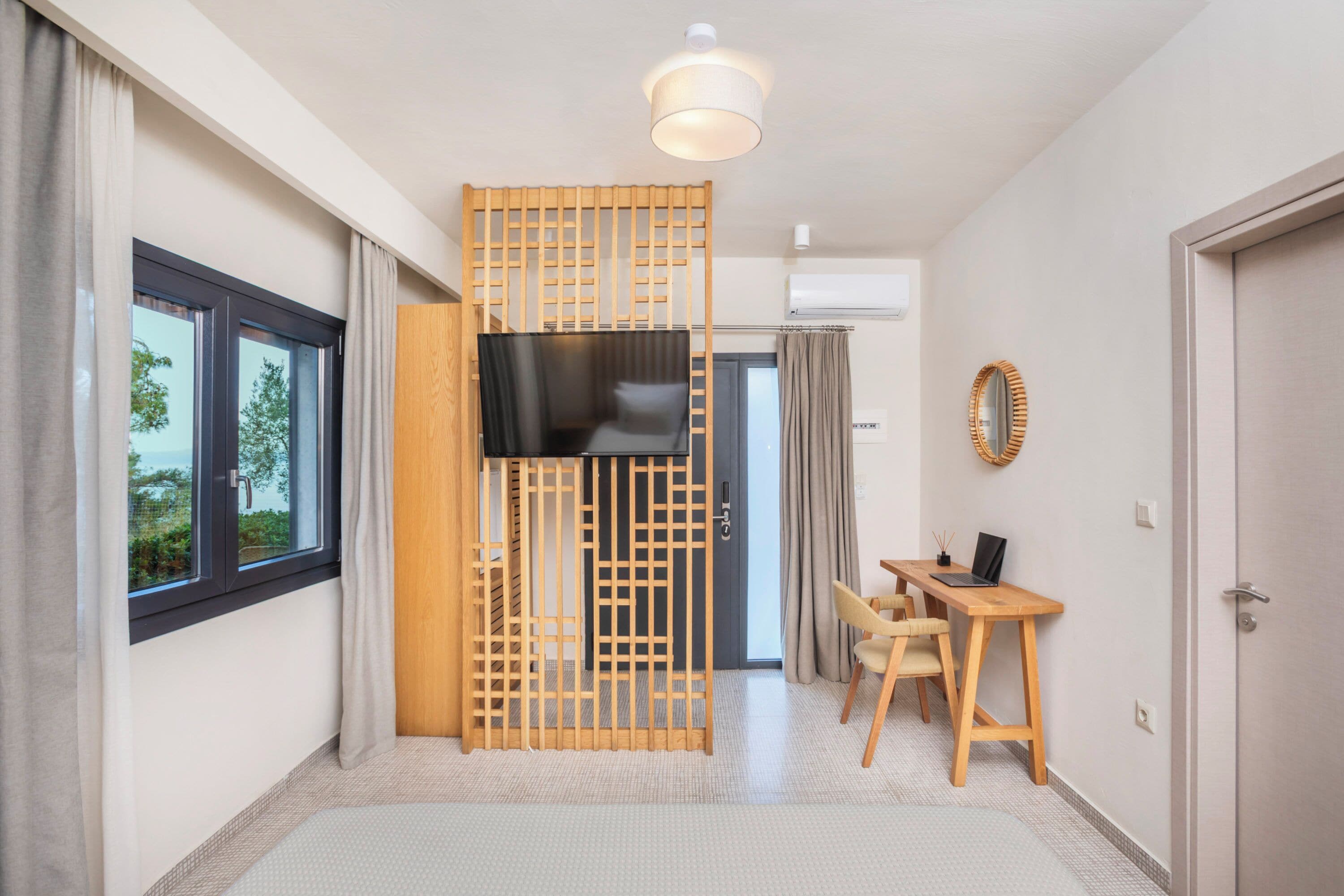 A modern hotel room with a large window, a TV, a desk with a chair, and a wooden partition.
