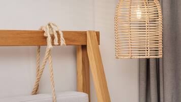 Une lampe en osier, posée sur un pied en bois auquel est attachée une corde, le tout adossé à un mur uni, avec un rideau gris en arrière-plan.