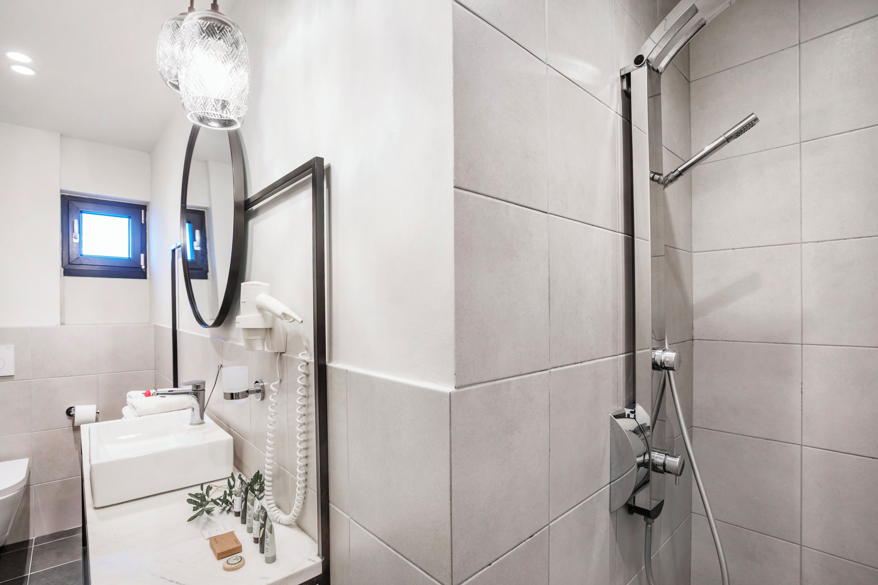 A modern bathroom with a large mirror, a sink, a handheld showerhead, and a toilet.