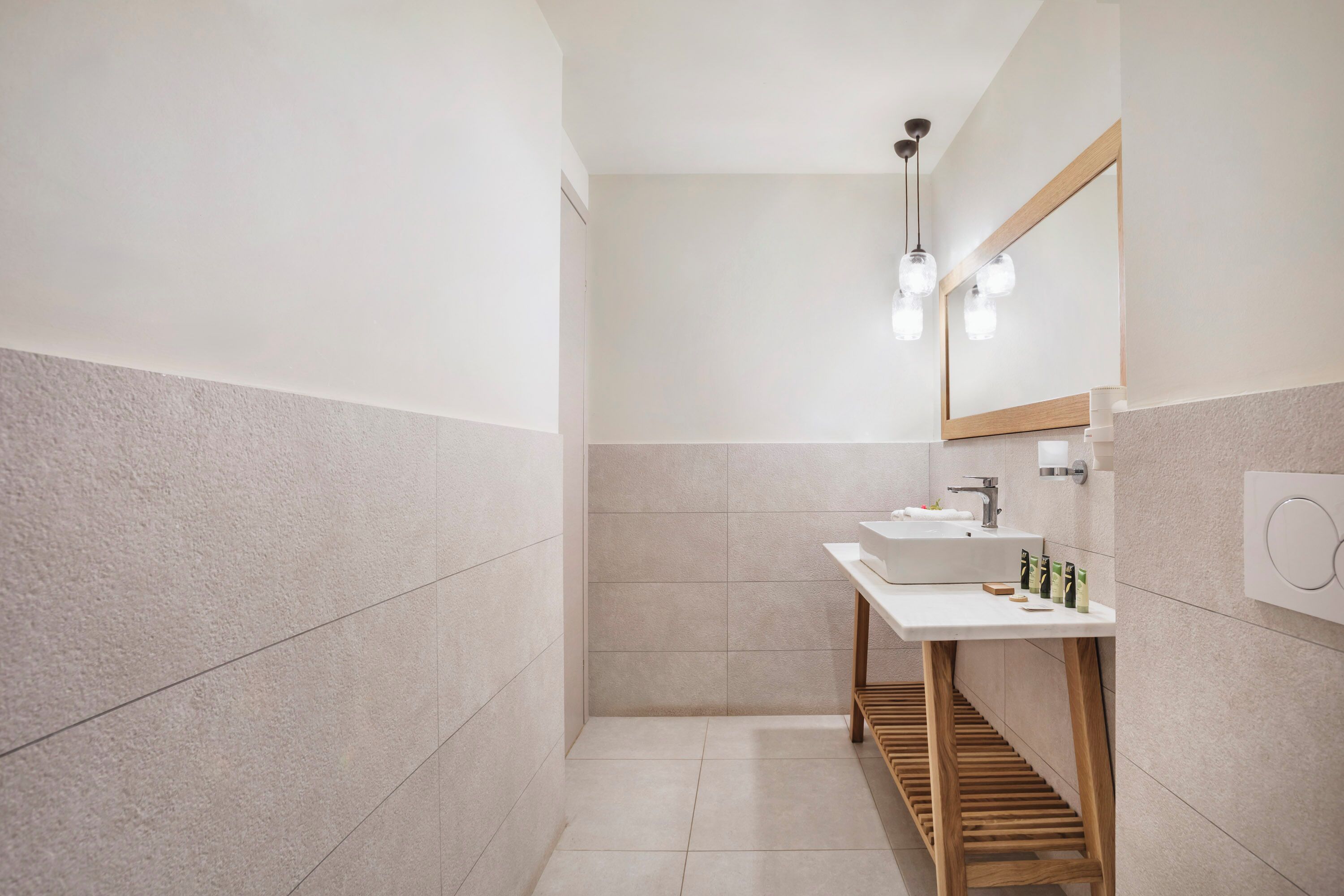 Un baño moderno con lavamanos blanco, espejo y banco de madera.